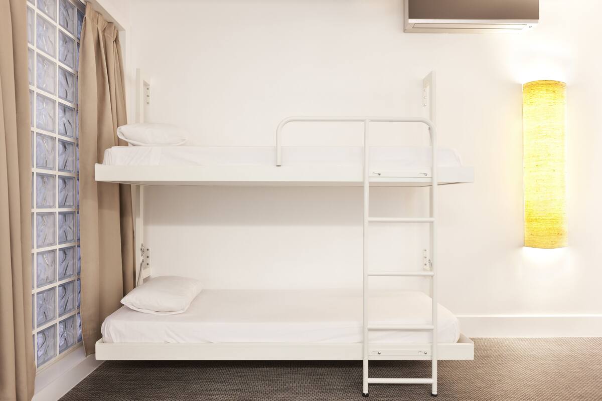 A bunk bed with a ladder, a window with curtains, and a wall-mounted light fixture.