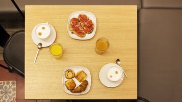Une table de petit-déjeuner avec des croissants, une assiette de jambon cru, une tasse de café et un verre de jus d’orange.