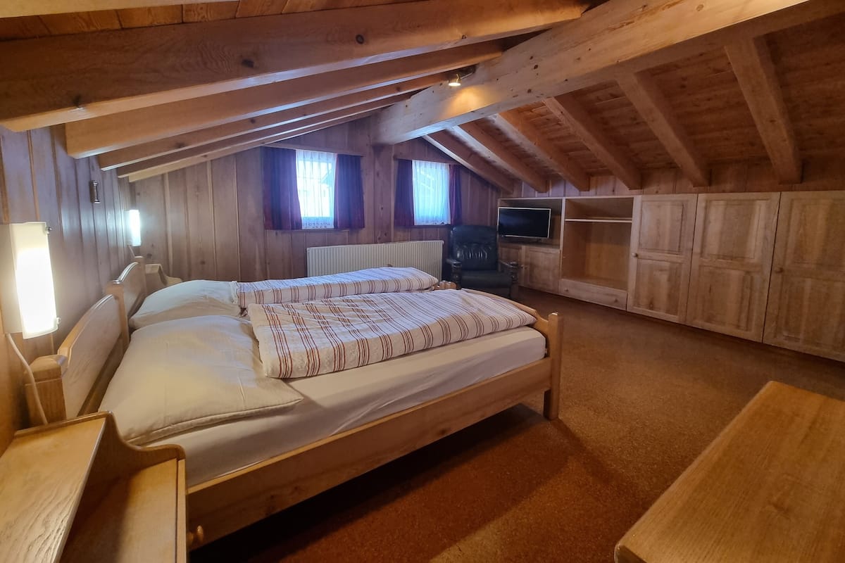 A wooden room with a bed, a chair, a TV, and a cabinet.
