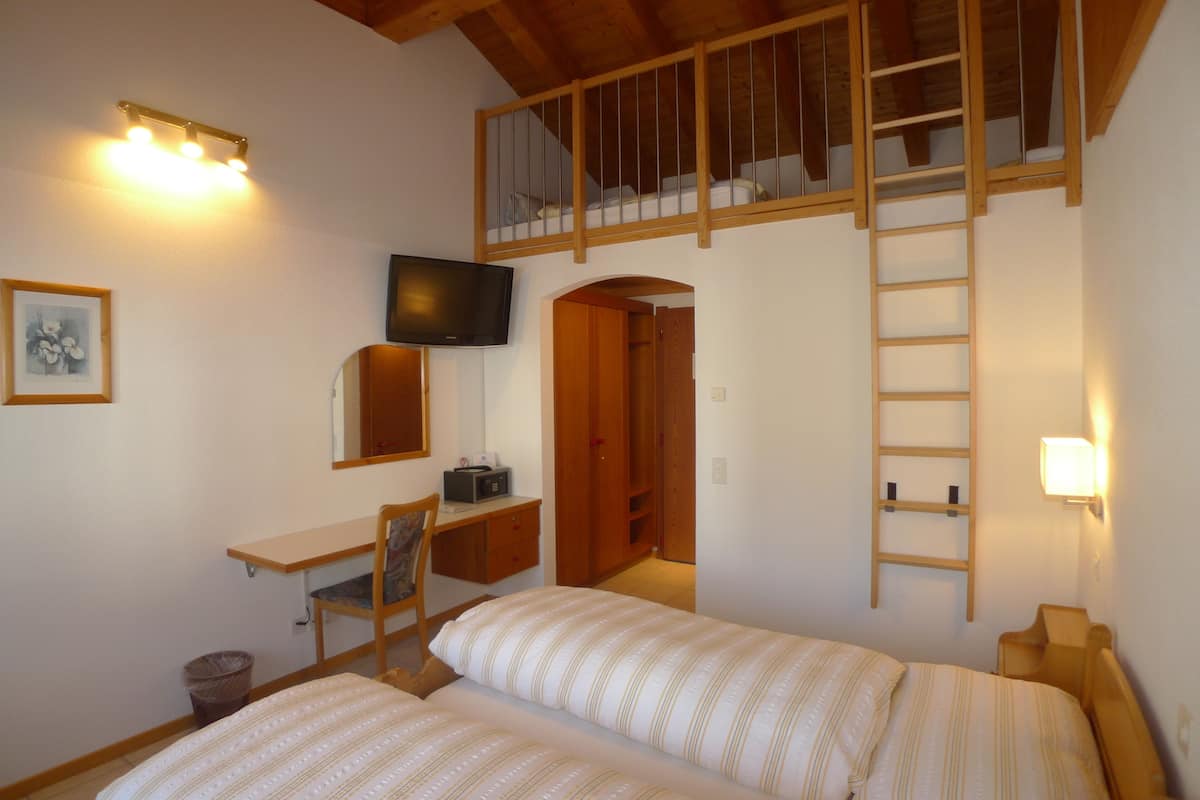 A bedroom with two beds, a desk, a chair, a TV, and a loft area with a ladder.