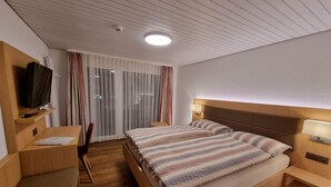 Hotellihuone, jossa on puinen sänky, työpöytä, jossa on televisio, ja ikkuna, jossa on verhot.