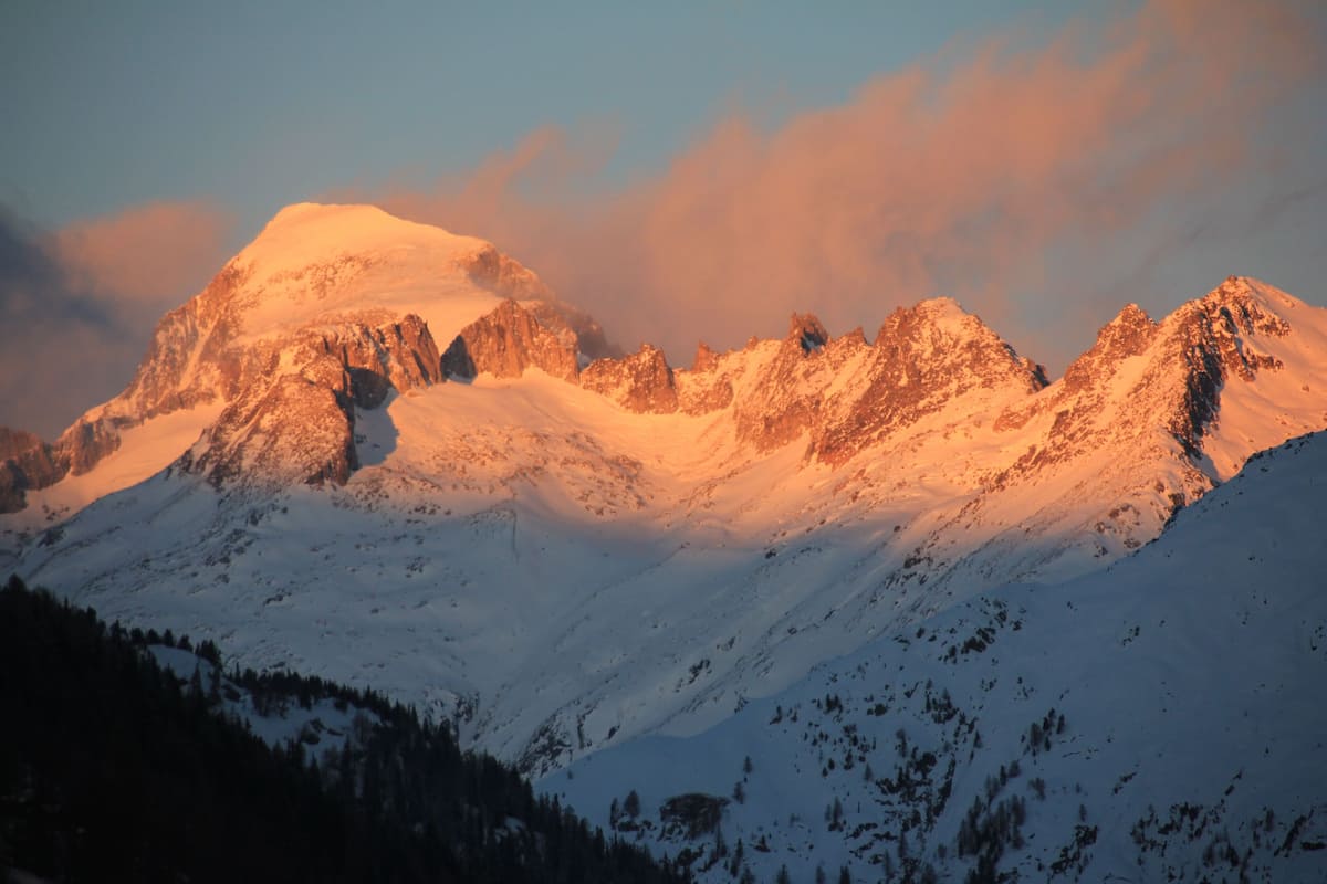A snow-covered mountain range with rugged peaks and a forested valley.