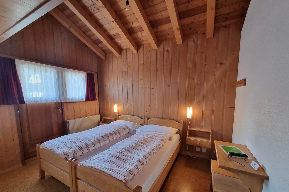 A wooden cabin bedroom with a bed, bedside tables, and a desk with a lamp.