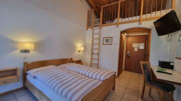 A bedroom with a wooden bed, a desk with a chair, a TV, and a ladder leading to a loft.