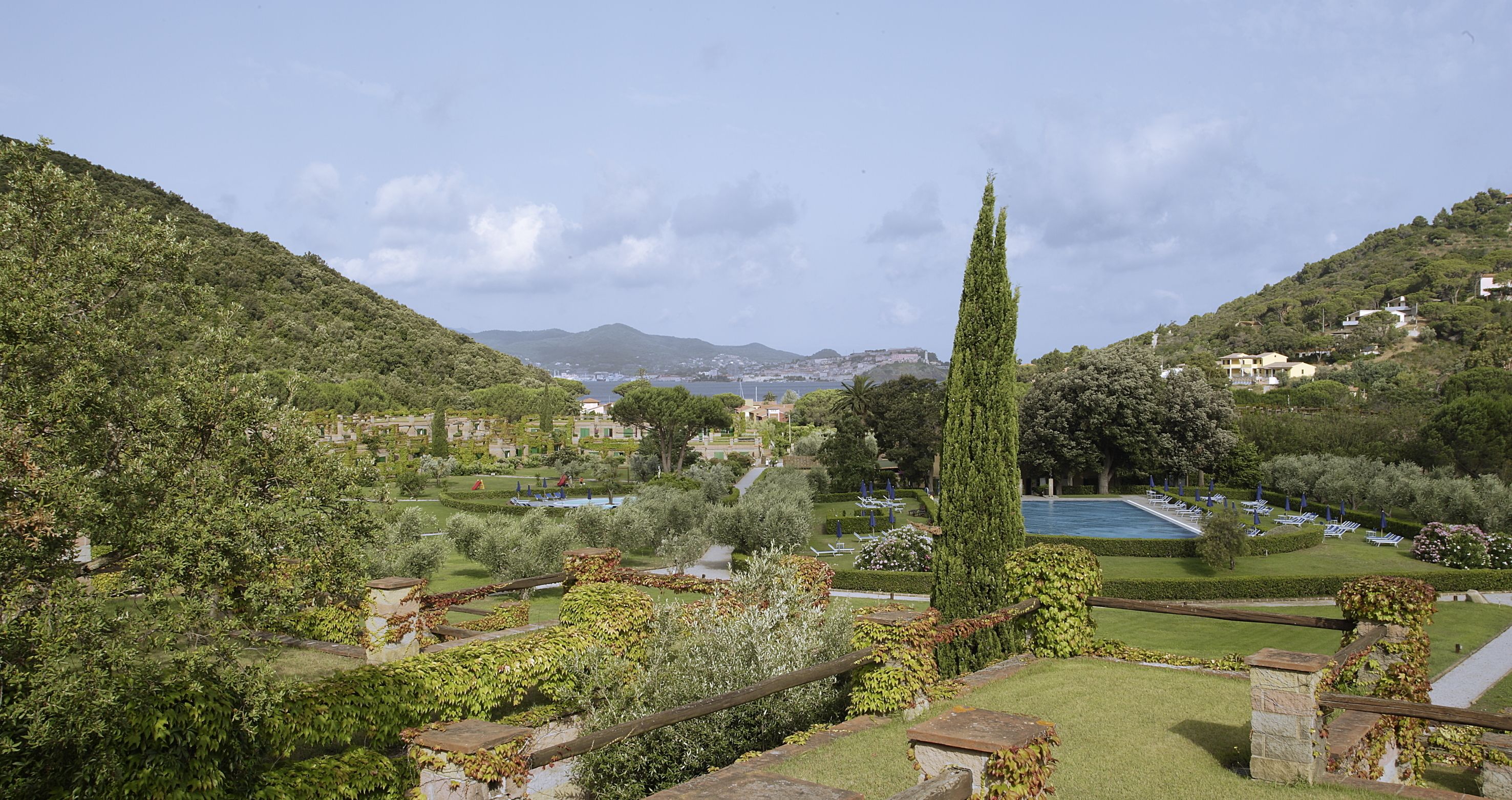 A landscaped garden with a pool, stone structures, and a view of a distant town.