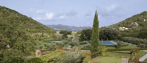 A landscaped garden with a pool, stone structures, and a view of a distant town.