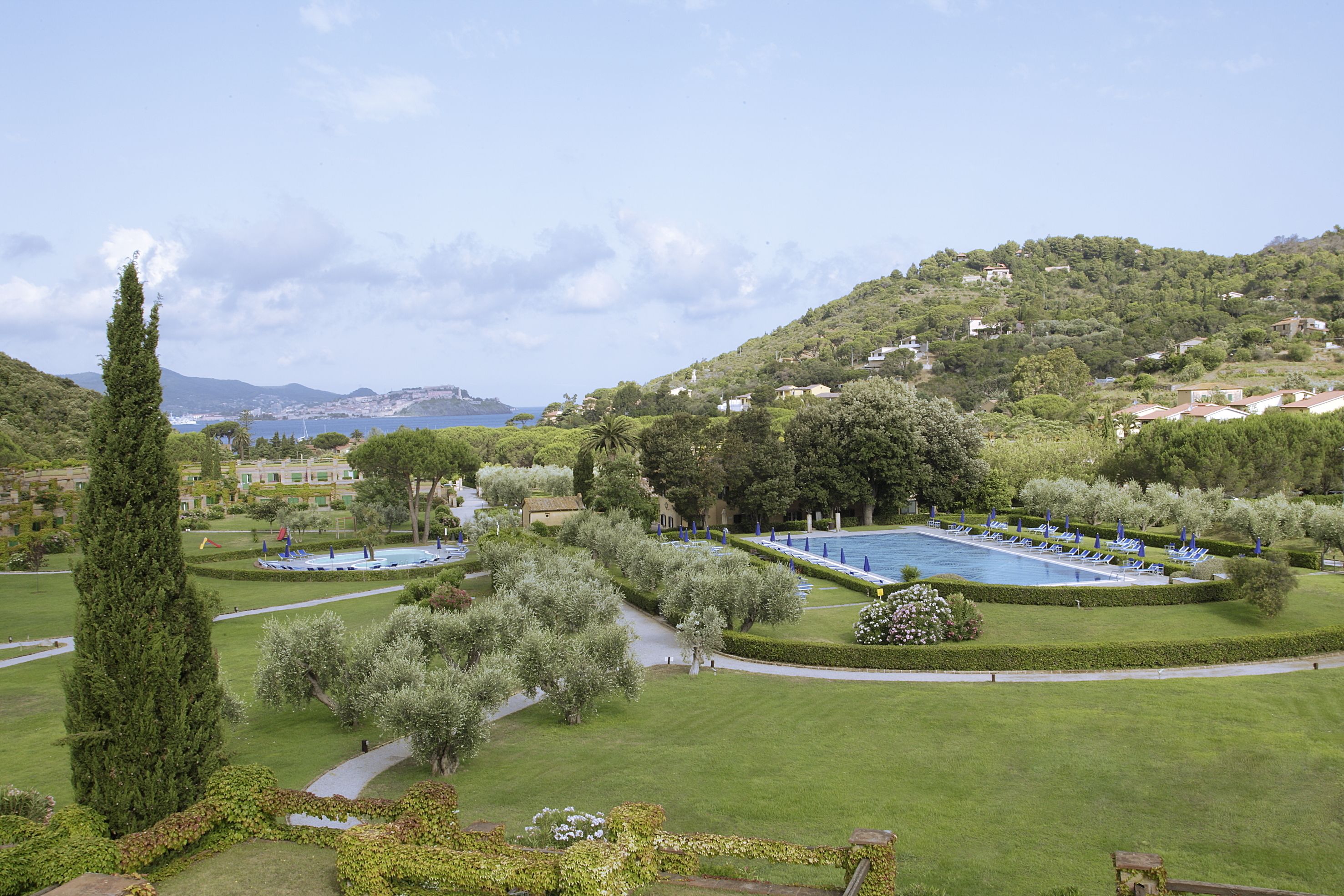 A landscaped garden with a pool, pathways, and a view of a hillside with buildings.
