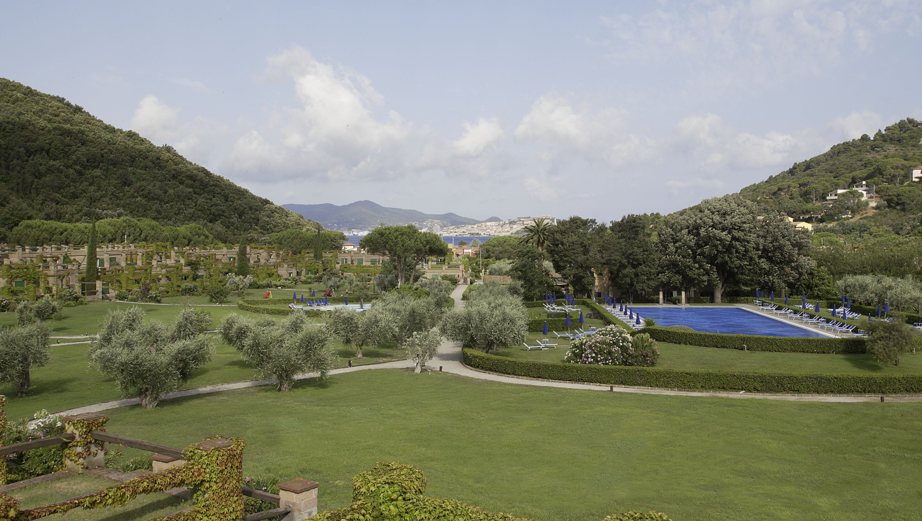 Um resort com piscina, gramados verdes e montanhas ao fundo.
