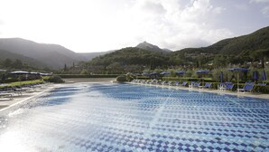 A large outdoor swimming pool with blue tiles, surrounded by lounge chairs and umbrellas, set against a backdrop of mountains and greenery. - Residenza Sant'Anna del Volterraio (Rio)