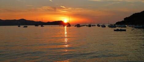A sunset over a calm body of water with several boats anchored.