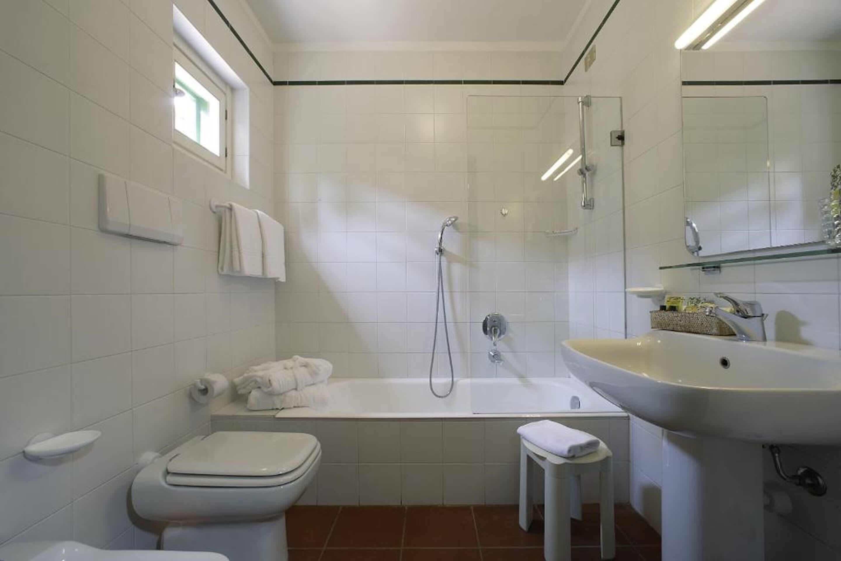 Et badeværelse med toilet, badekar, vask og en lille skammel.