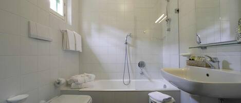 Un baño con inodoro, bañera, lavamanos y un taburete pequeño.