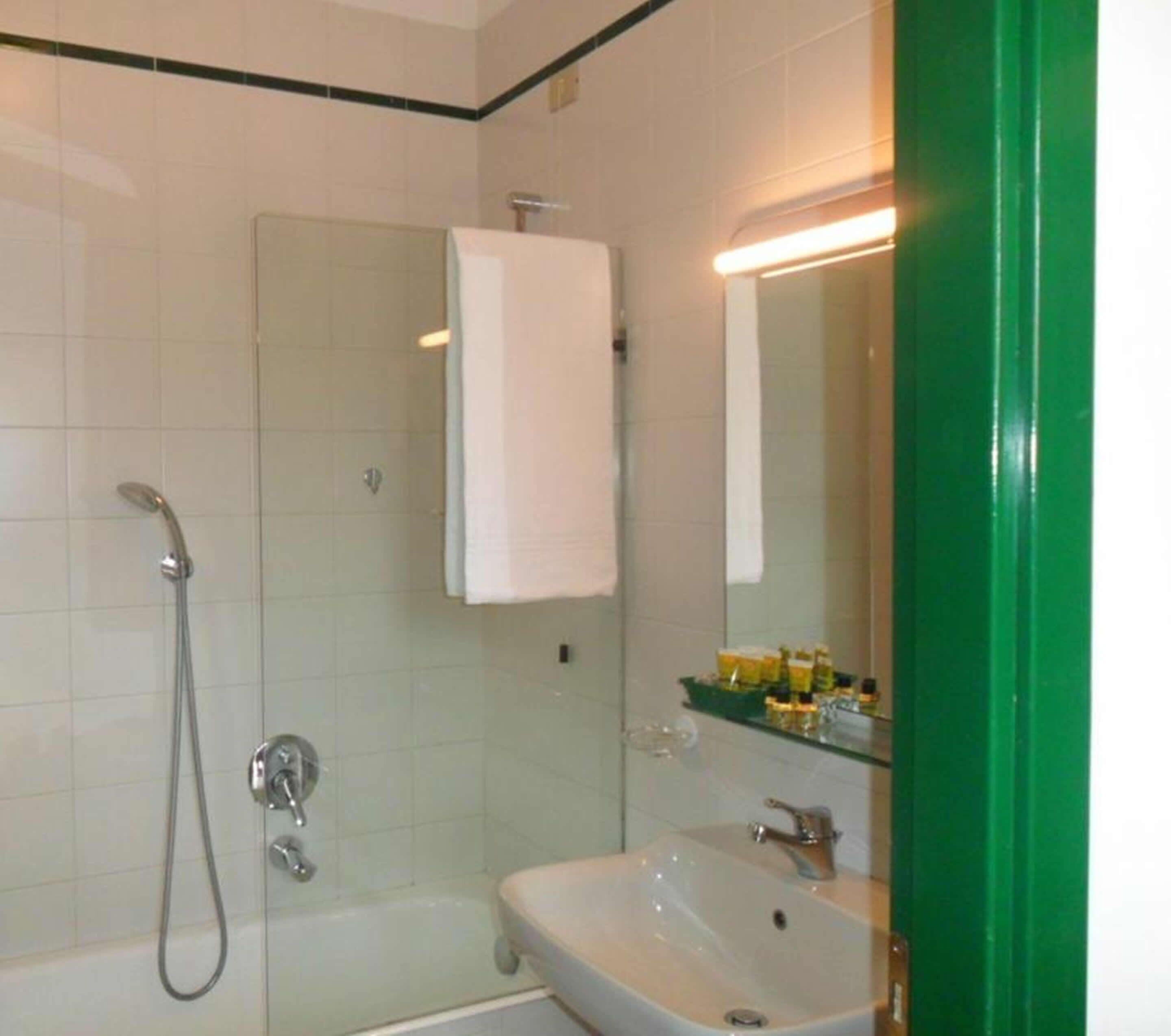 Un baño con ducha, lavamanos, espejo y toallero.