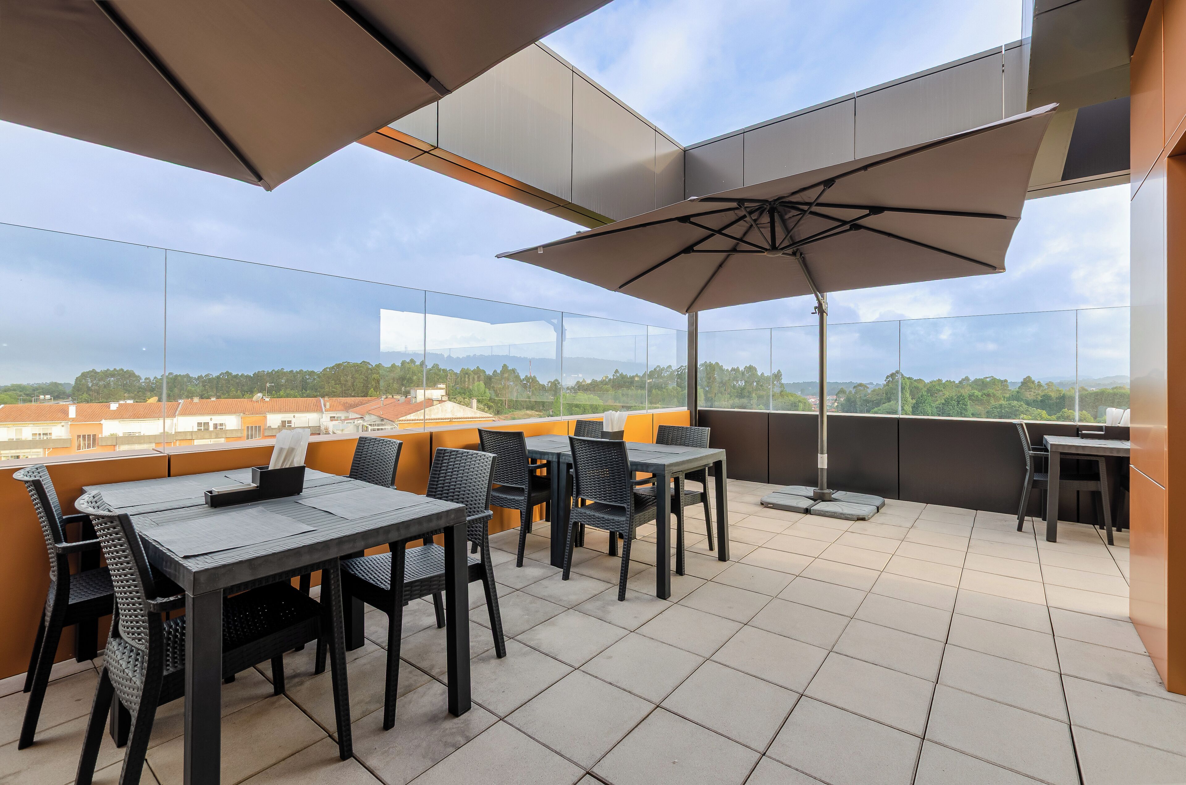 A rooftop terrace with outdoor seating, including tables and chairs, and a large umbrella providing shade.