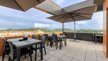 A rooftop terrace with outdoor seating, including tables and chairs, and a large umbrella providing shade.