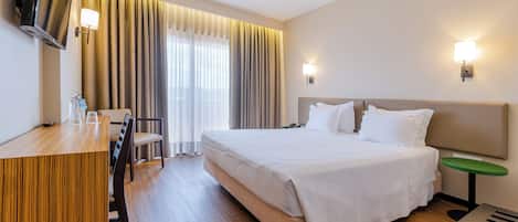 A hotel room with a large bed, a desk with a chair, a TV mounted on the wall, and two wall-mounted lamps.