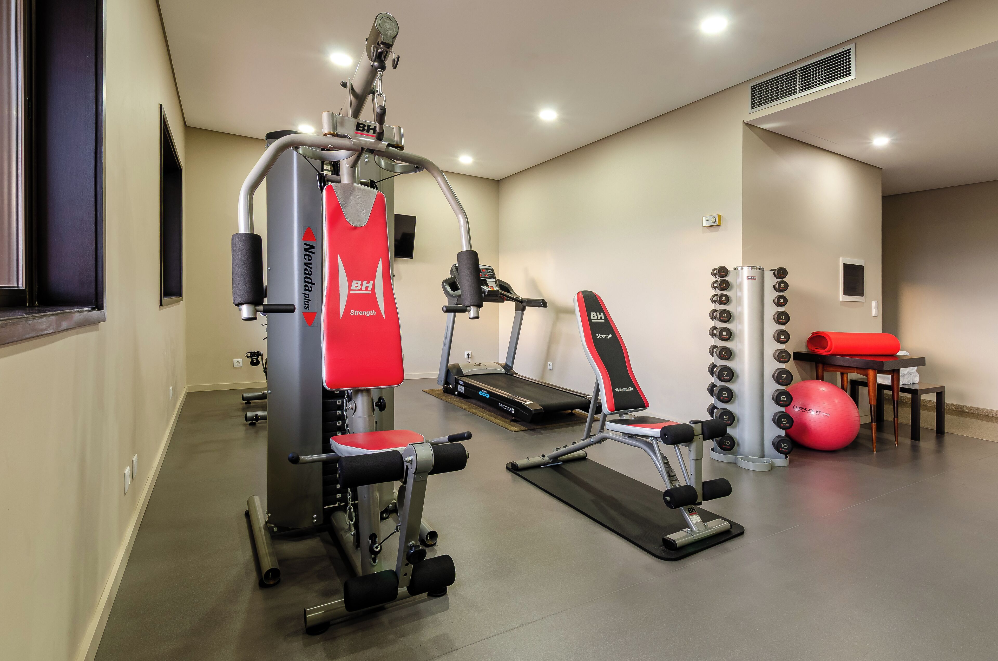 A gym with exercise equipment, a treadmill, and a red exercise ball.