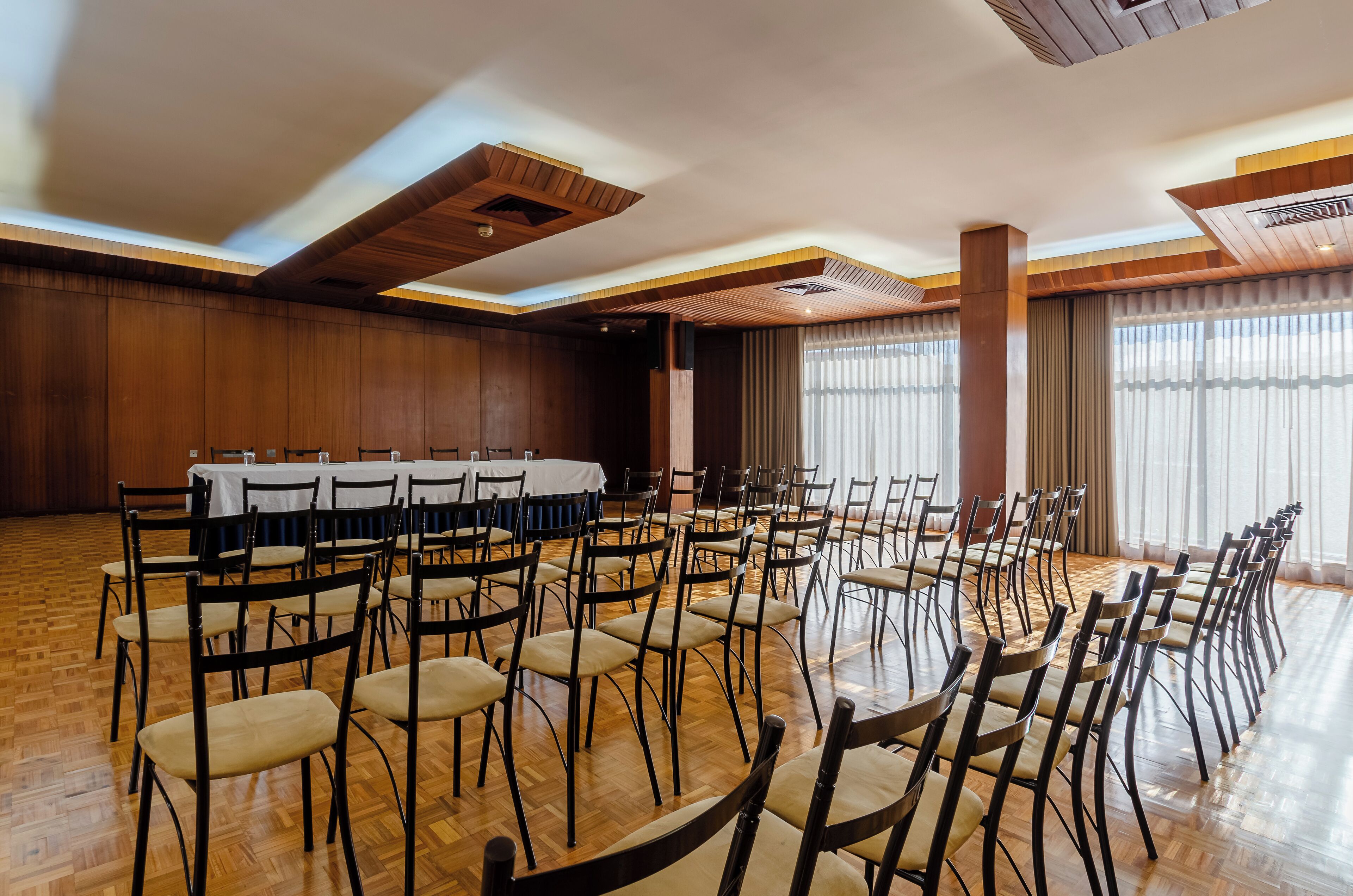 Ein Konferenzraum mit einem langen Tisch, Stühlen, Holzböden und großen Fenstern mit Vorhängen.