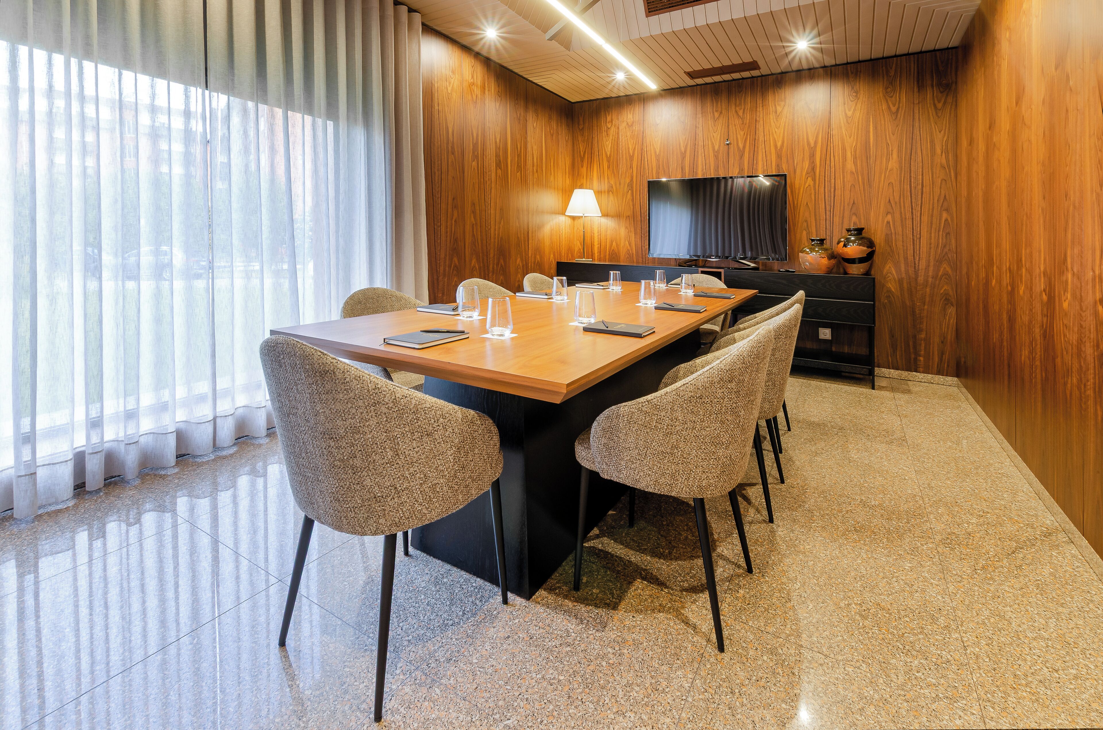 A conference room with a wooden panel wall, a large TV, and a long table with chairs.