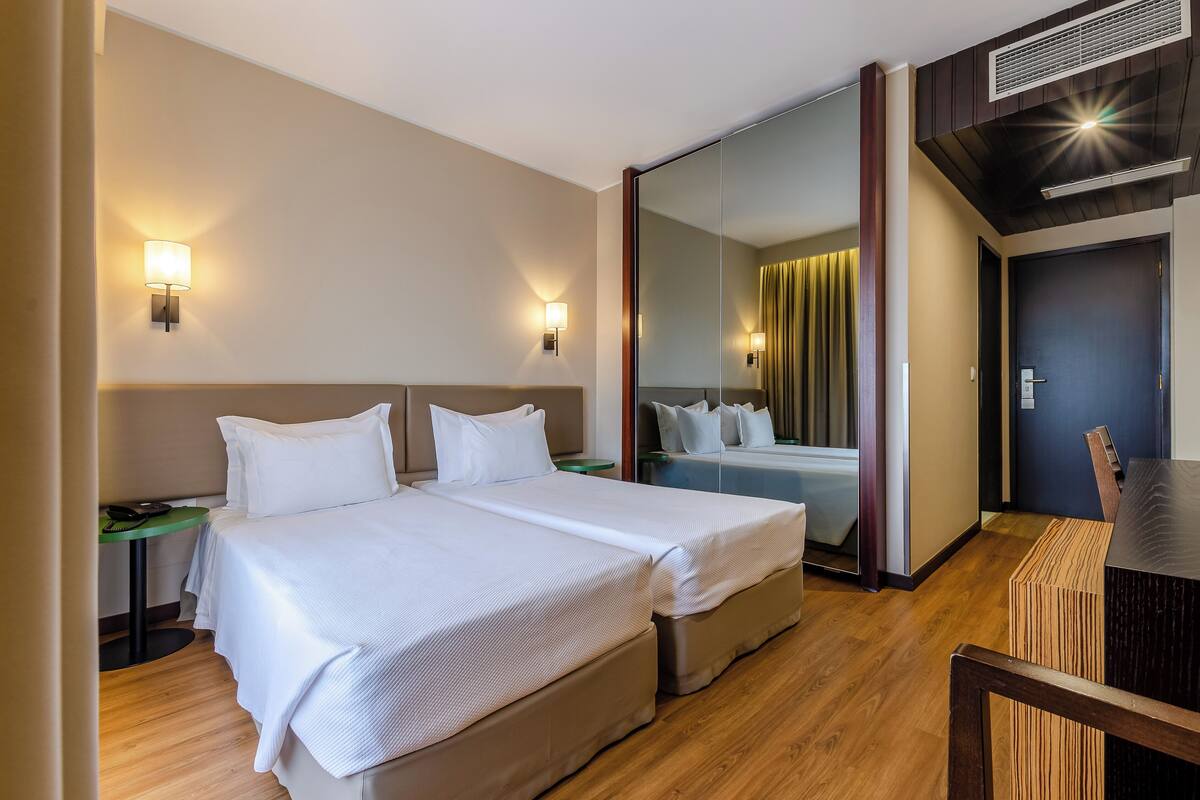 Une chambre d’hôtel avec deux lits, une petite table, une chaise, un miroir et une porte.