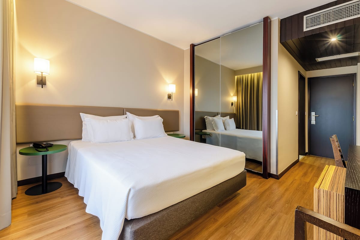 Une chambre d’hôtel avec un grand lit, des tables de chevet, un miroir et un plancher en bois.