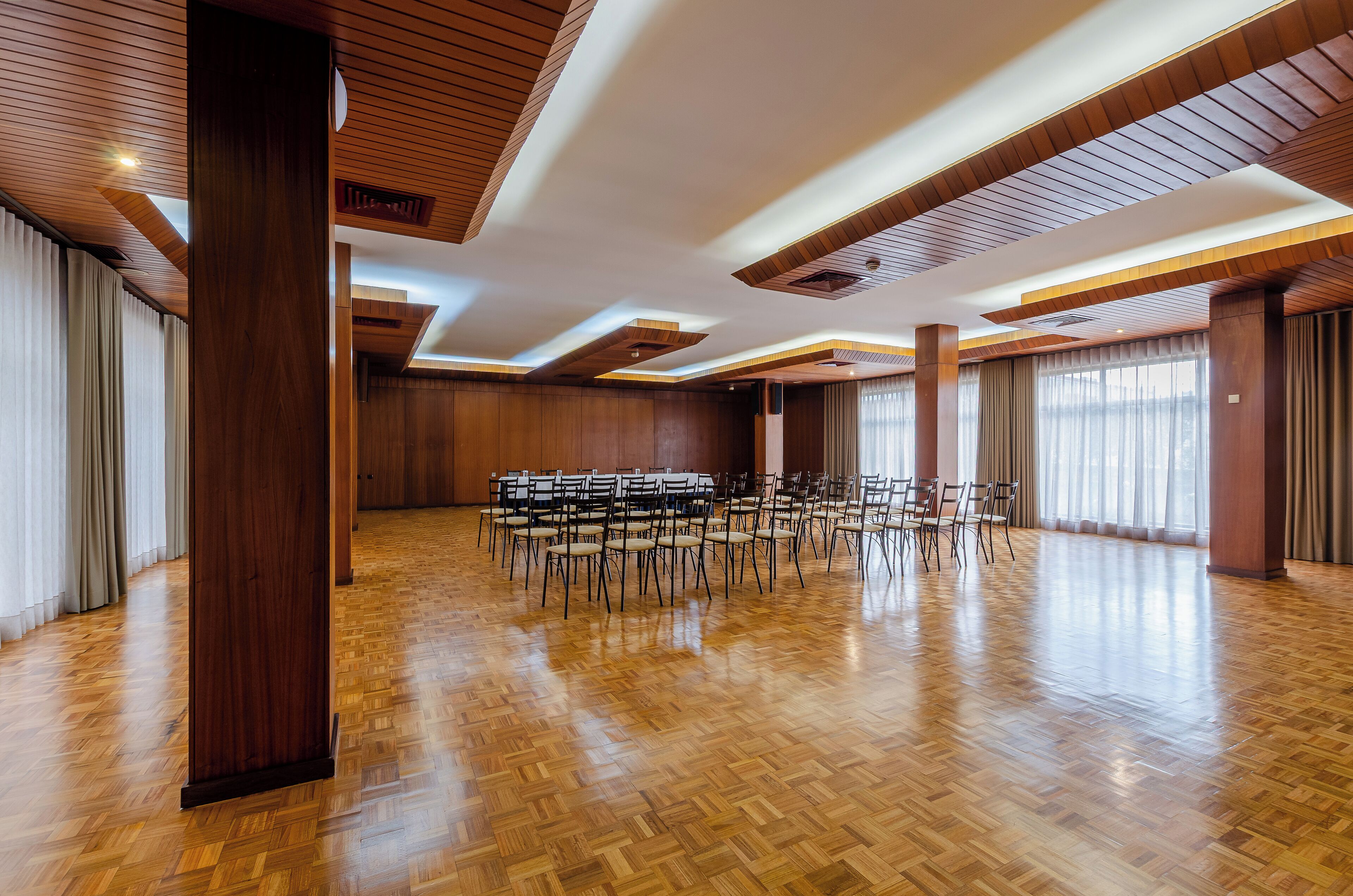 A spacious hall with wooden flooring and ceiling, arranged with rows of chairs for seating.