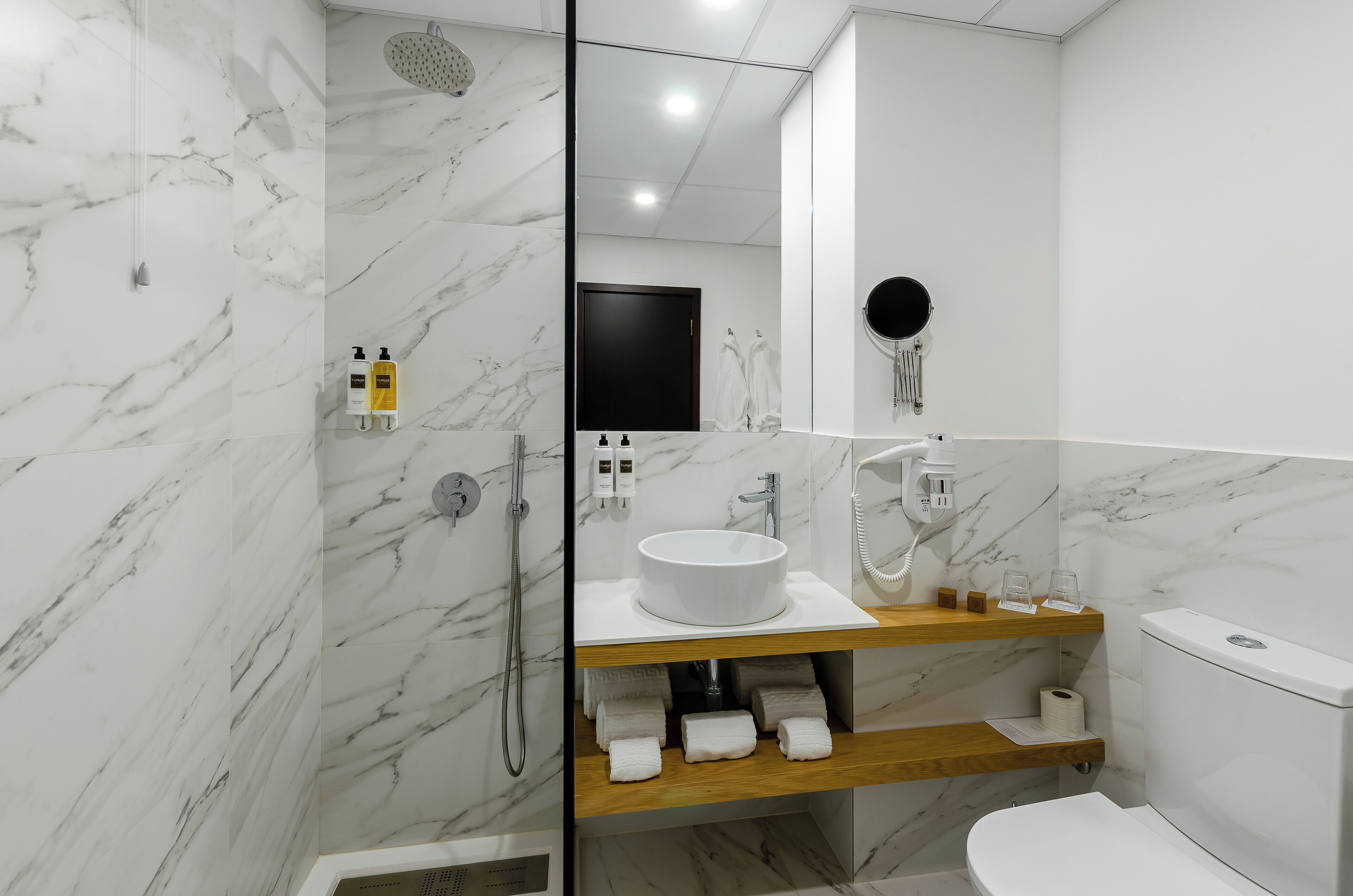 A modern bathroom with a marble wall, a round sink, a toilet, and a shower.