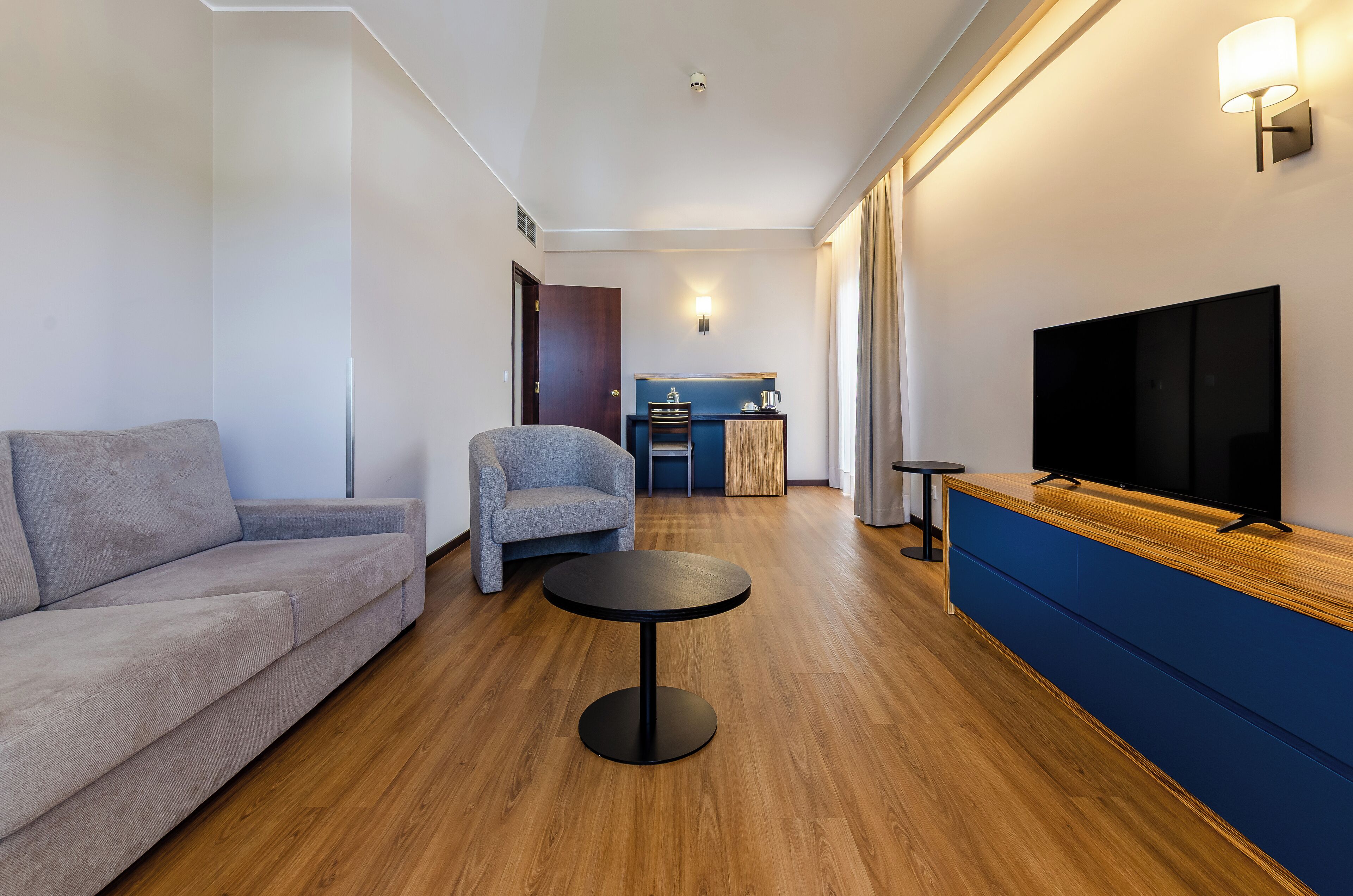 Ein modernes Wohnzimmer mit einer Couch, einem Sessel, einem runden Couchtisch und einem Fernseher auf einem Holzschrank.