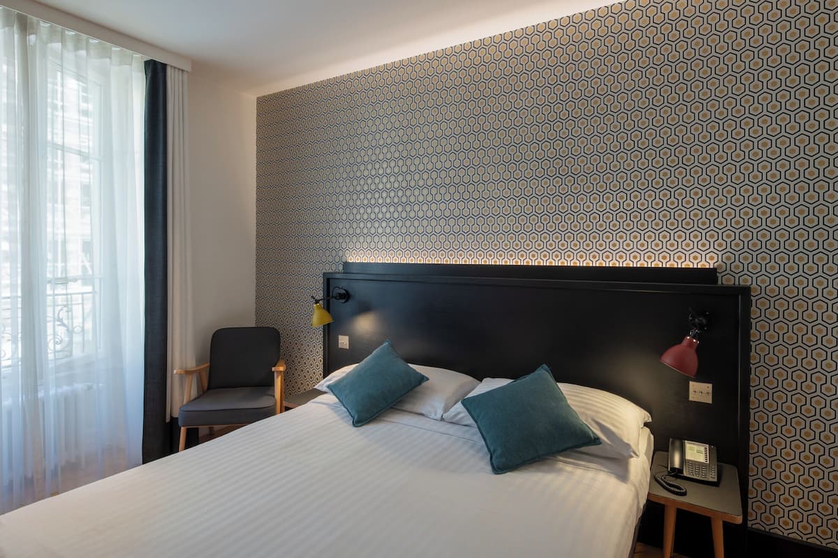 A hotel room with a large bed, two pillows, a bedside table with a phone, and a chair.