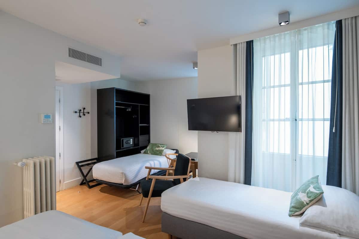 A hotel room with a bed, a desk, a wardrobe, a television, and a window with curtains.