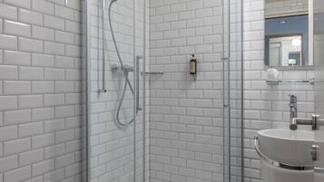 Un baño moderno con ducha de vidrio, azulejos blancos tipo metro, un lavamanos blanco y un inodoro.