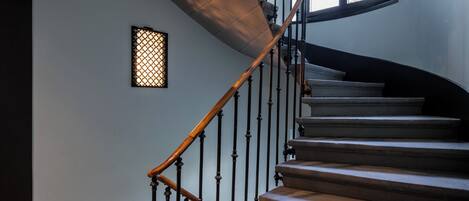 Una escalera con barandilla de madera y balaustradas negras, que conduce a un rellano con un ventanal decorativo.