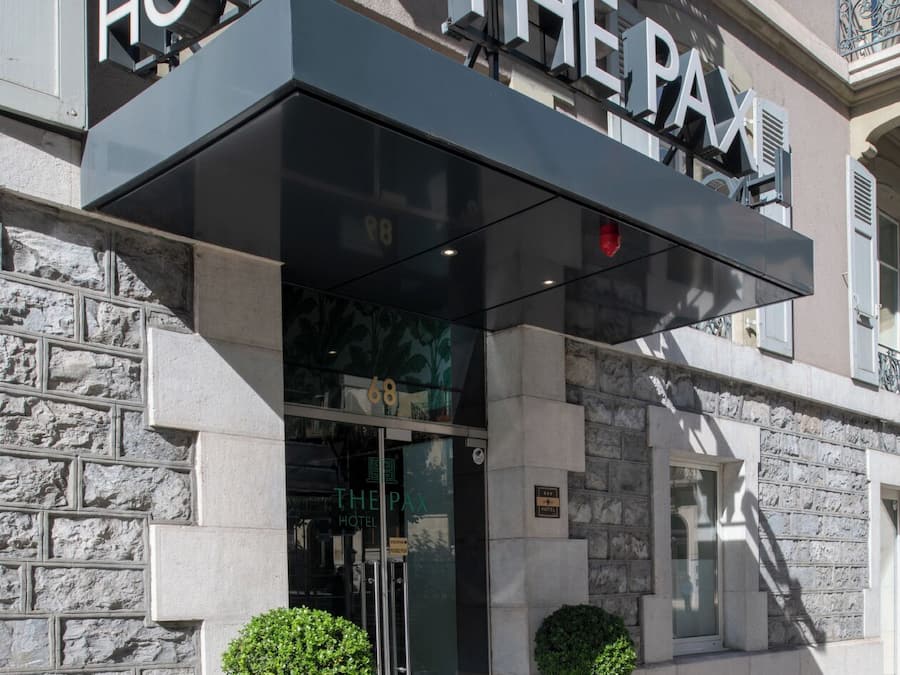 Exterior del Hotel PAX, con fachada de piedra, una entrada moderna con puertas de vidrio y dos macetas en la entrada.
