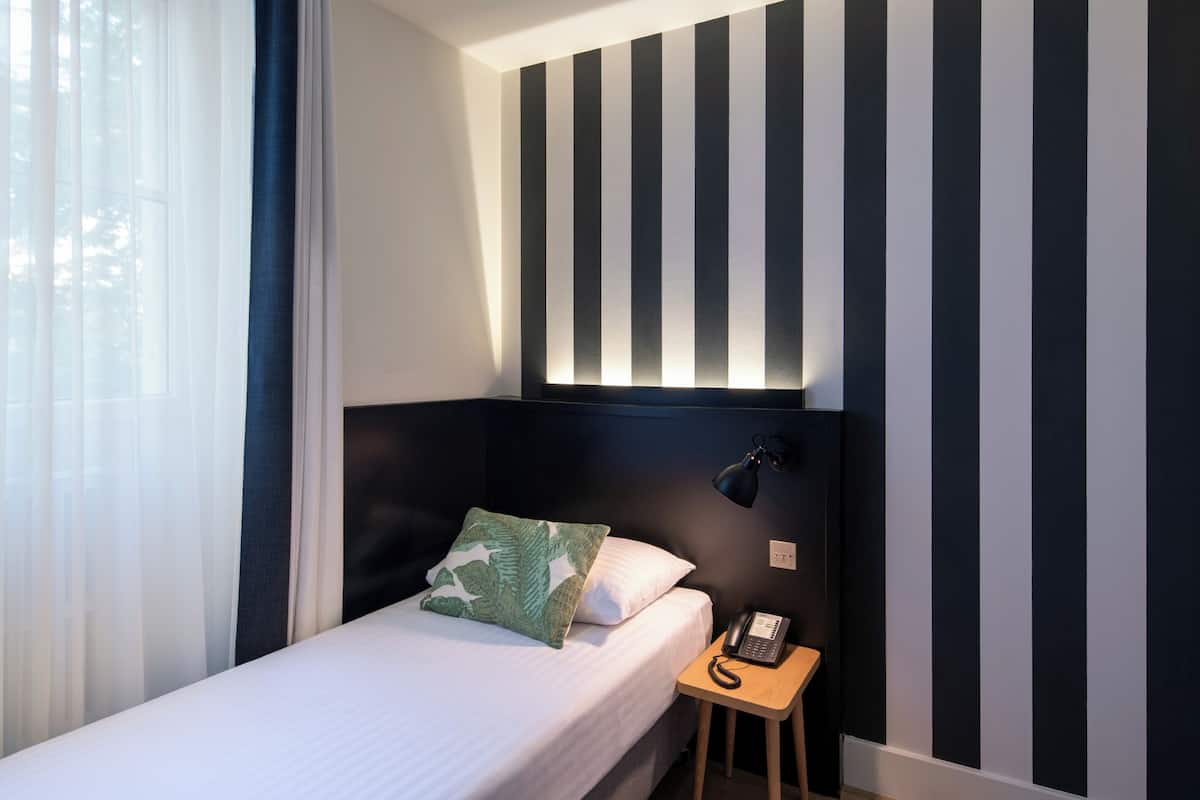 A hotel room with a bed, a bedside table with a telephone, and a wall-mounted lamp.