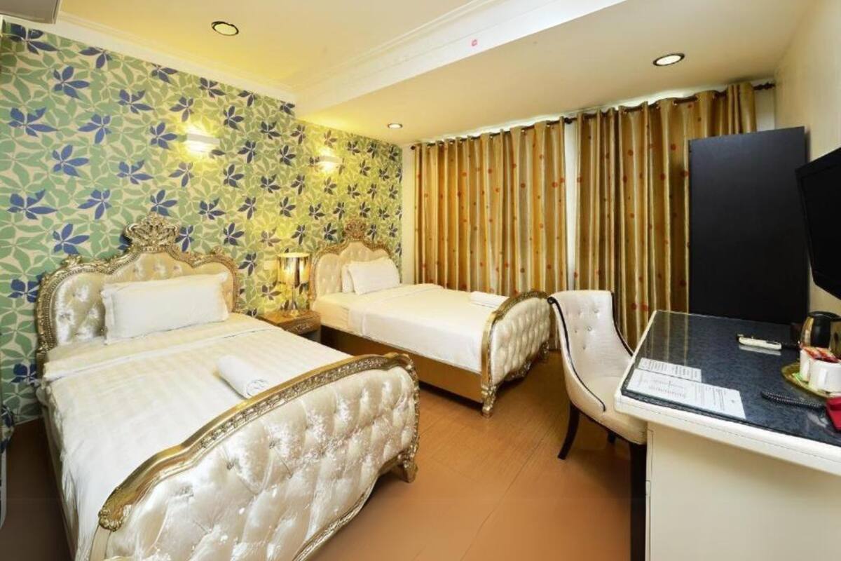Quarto de hotel com duas camas, uma escrivaninha com computador e uma televisão.