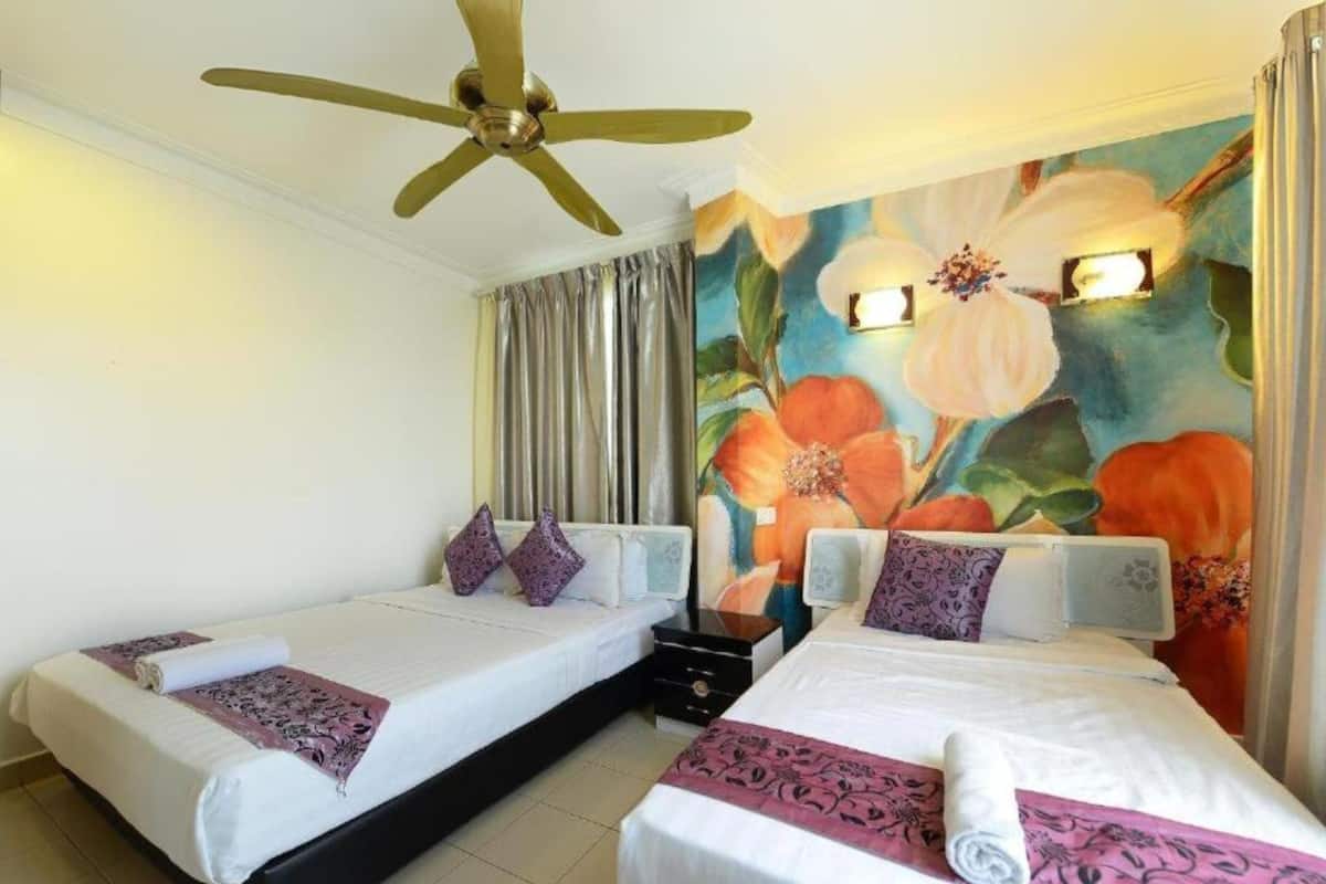 Quarto de hotel com duas camas, um ventilador de teto, um mural floral e uma janela com cortinas.
