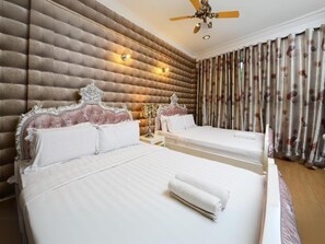 Habitación de hotel con dos camas, ventilador de techo y ventana grande con cortinas.