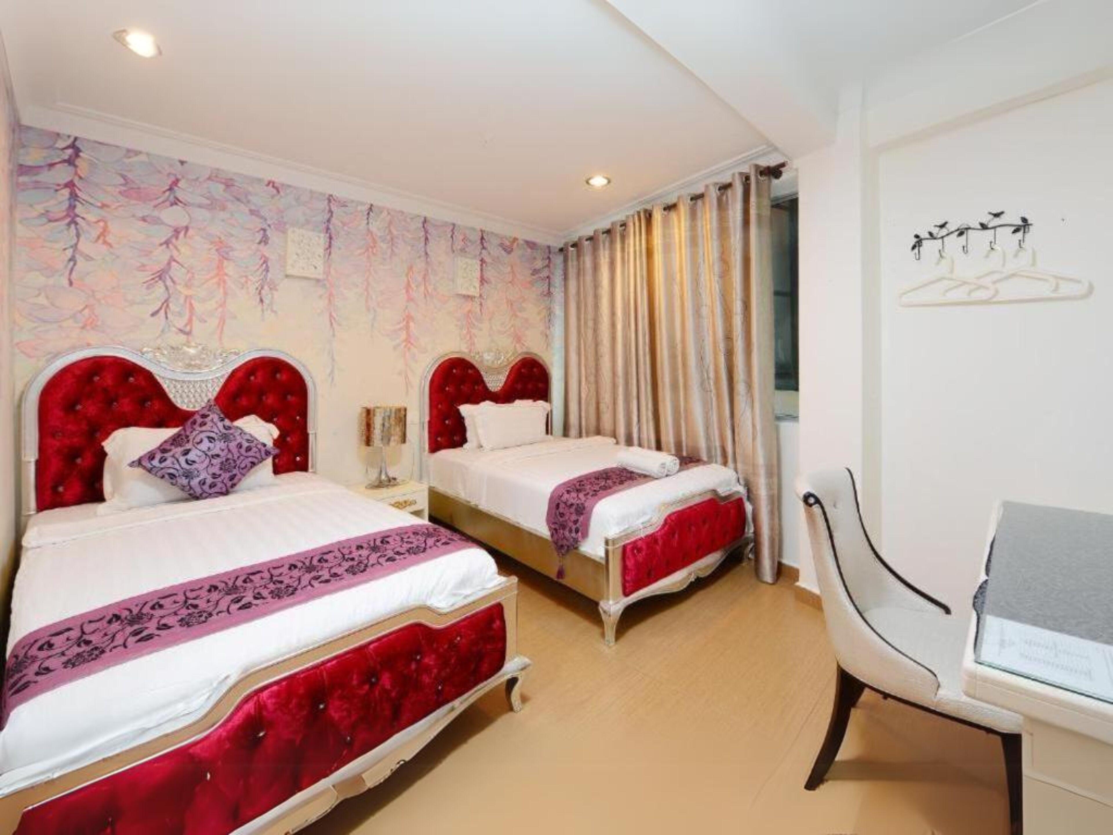 Ein Hotelzimmer mit zwei Betten, jeweils mit roten Kopfteilen und weißer Bettwäsche. In der Ecke befindet sich ein Sessel und ein kleiner Tisch.