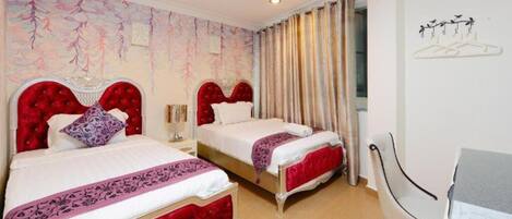 Ein Hotelzimmer mit zwei Betten, jeweils mit roten Kopfteilen und weißer Bettwäsche. In der Ecke befindet sich ein Sessel und ein kleiner Tisch.