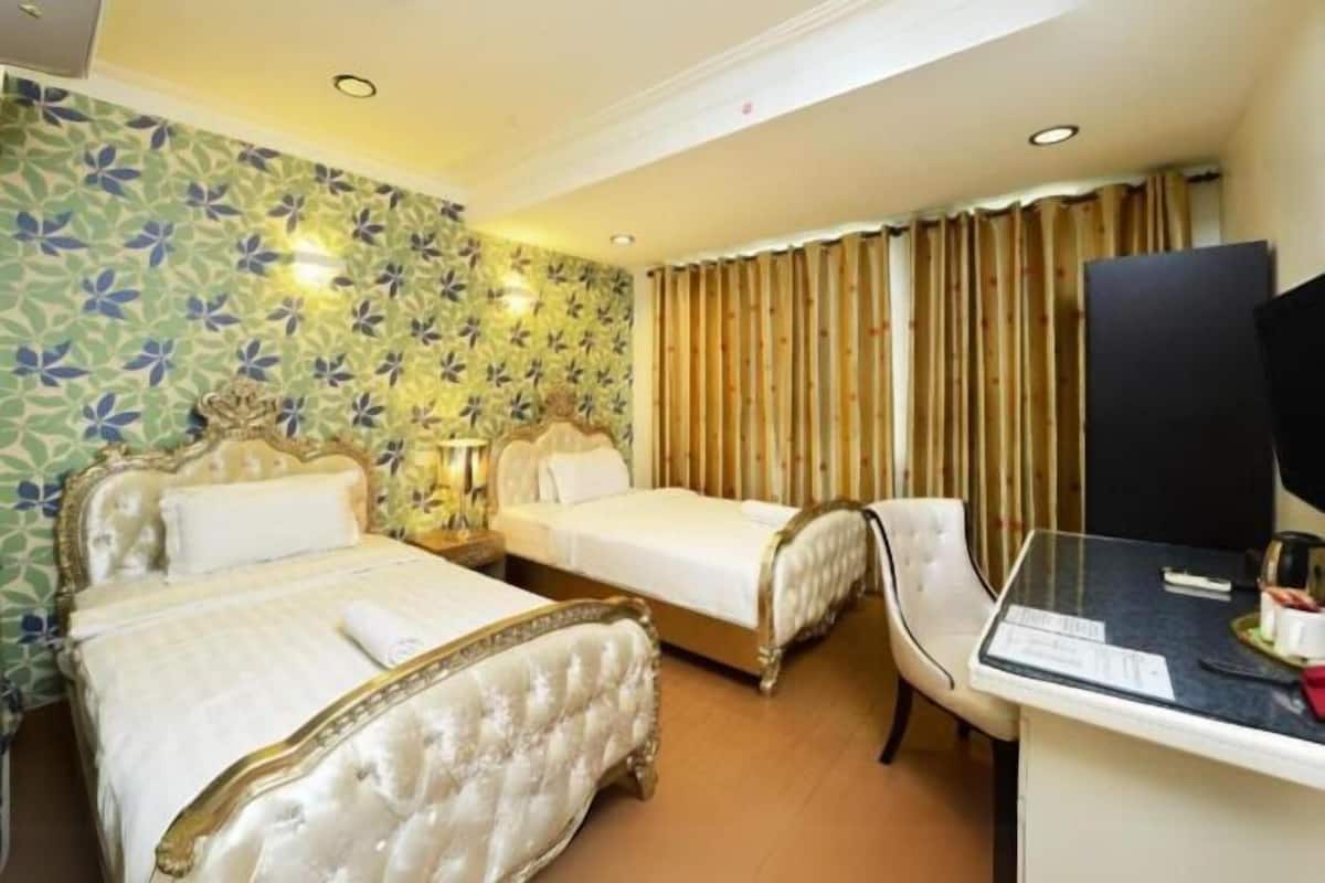 Quarto de hotel com duas camas, uma escrivaninha, uma cadeira e uma televisão.