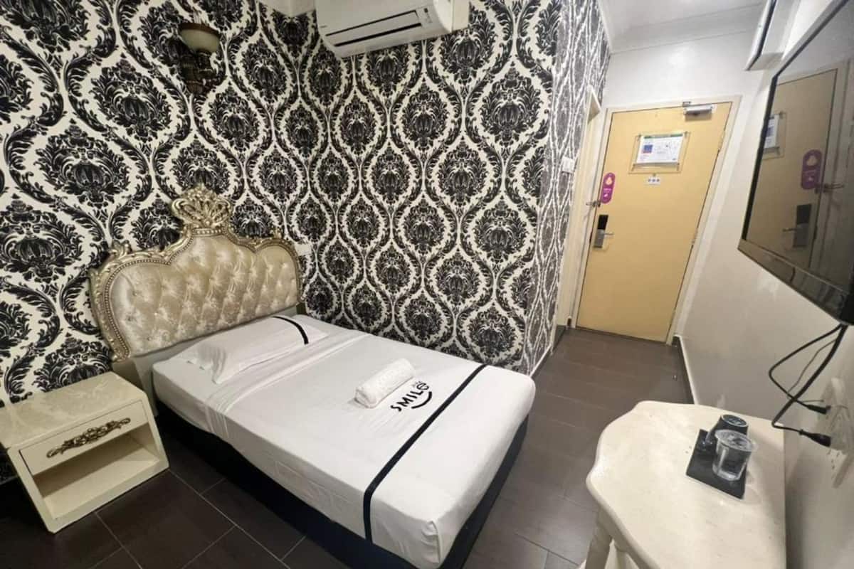 Quarto de hotel com uma cama, uma pequena mesa de cabeceira, um espelho e uma parede com papel de parede estampado.