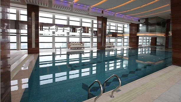 Ein Innenpool mit klarem Wasser, umgeben von großen Fenstern und modernen Möbeln.