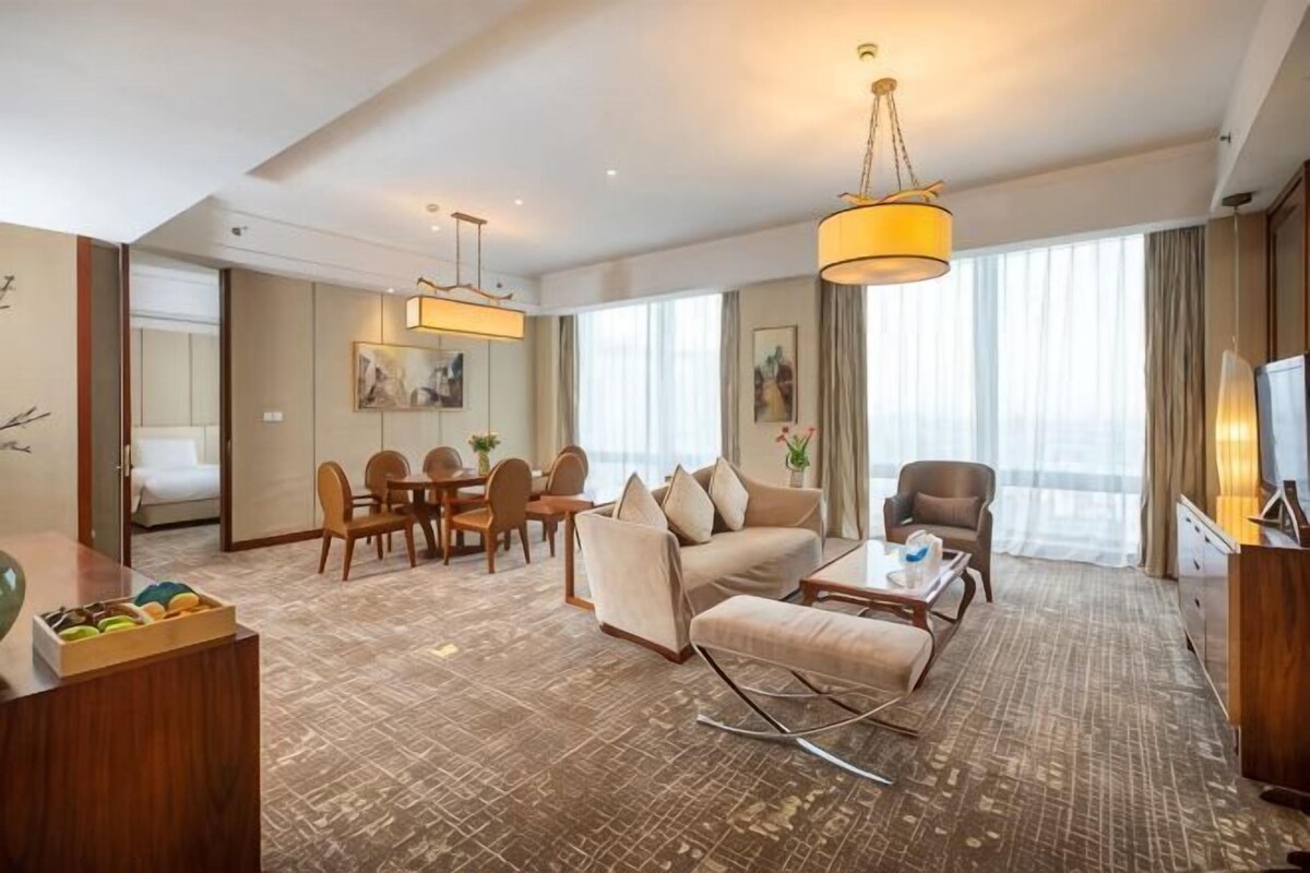 A hotel room with a dining area, a sofa set, a TV, and a large window.