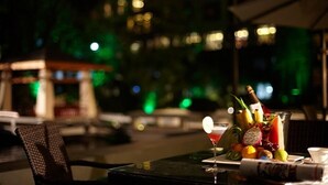 Ein Essbereich im Freien mit einem Tisch für zwei Personen, komplett mit einem Cocktail, Obst und einer Champagnerflasche.