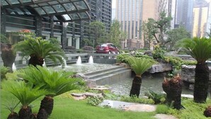 Ein angelegter Garten mit Wasserspiel, Palmen und einem in der Nähe geparkten roten Auto.