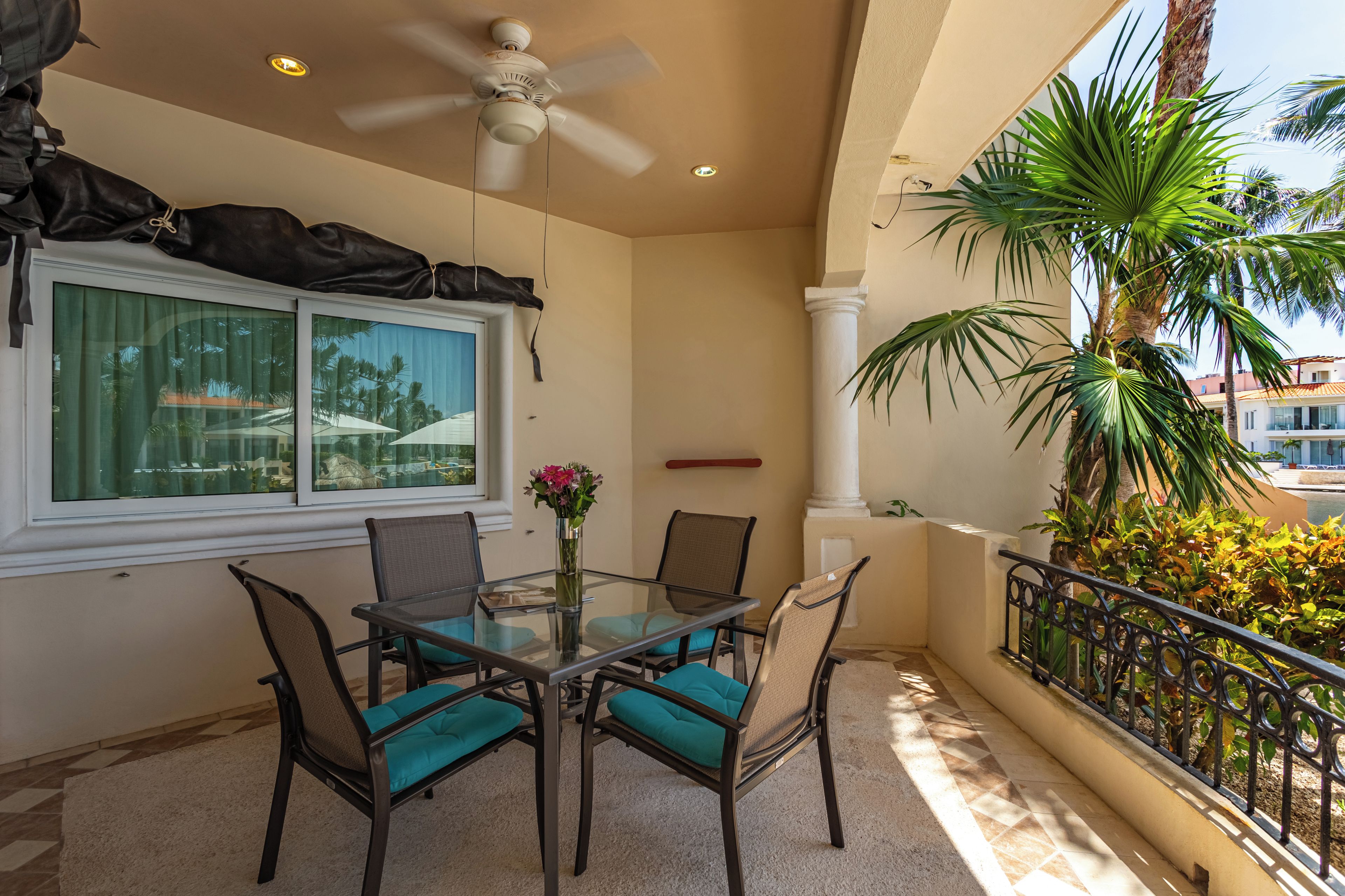 Un balcon avec une table et des chaises, un ventilateur de plafond et une vue sur les palmiers.