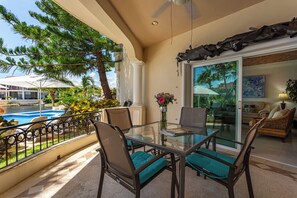 Een balkon met een glazen tafel, stoelen en uitzicht op een zwembad.