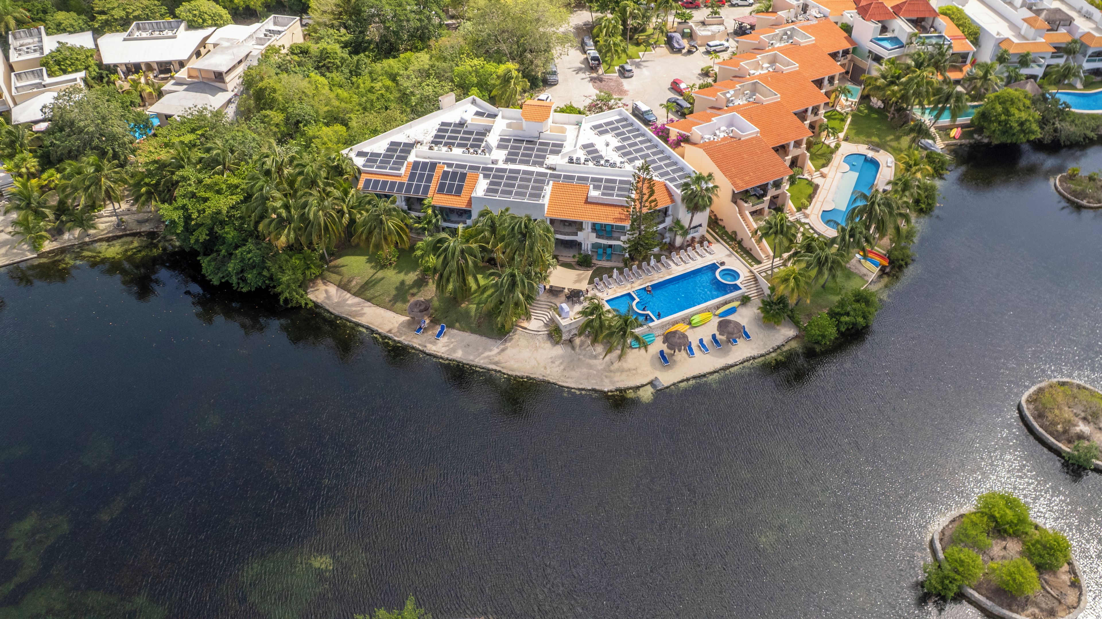 An aerial view of a resort with a swimming pool, solar panels, and a dock.