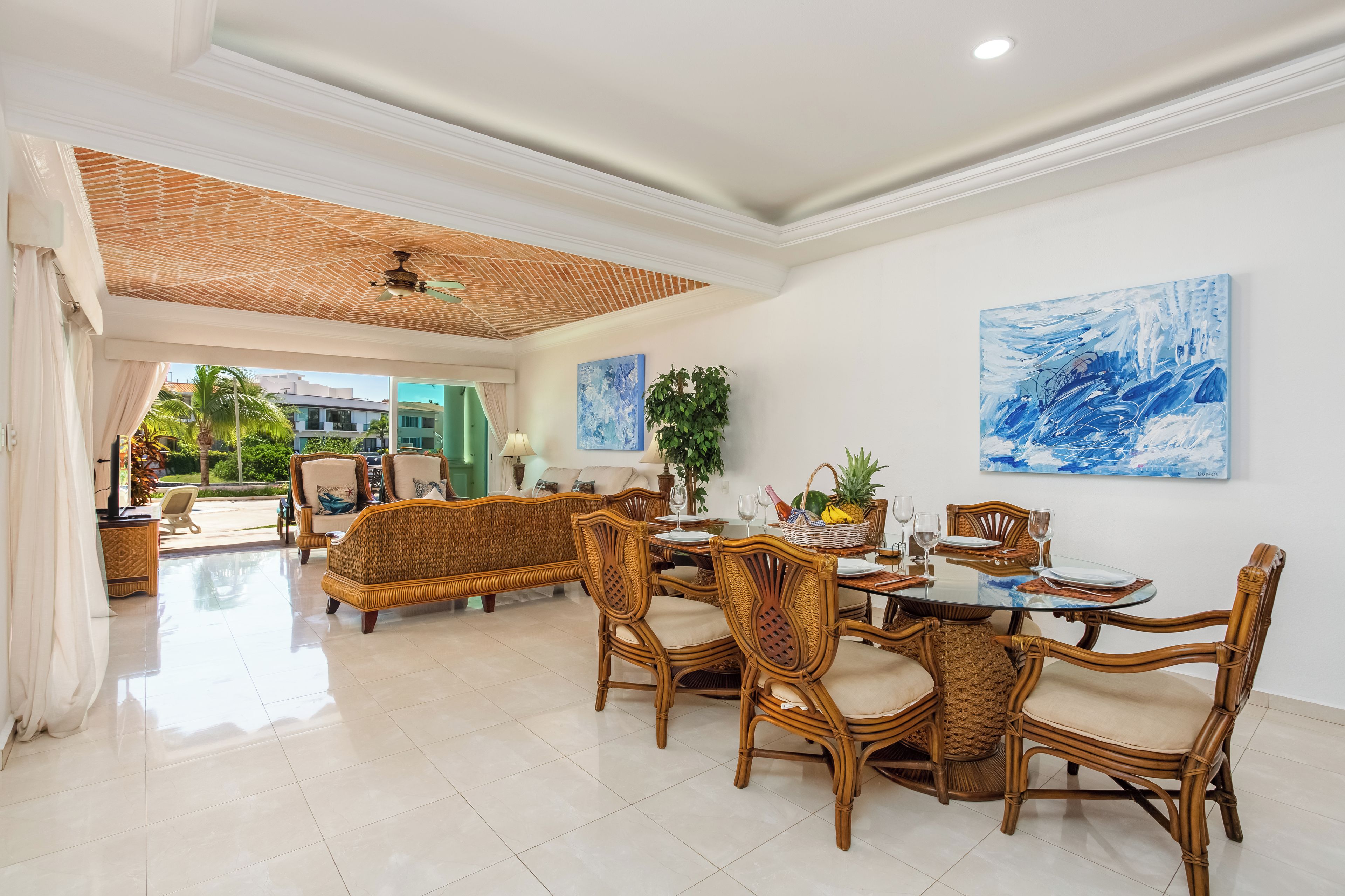 A spacious dining area with wicker furniture, a glass table, and artwork on the walls.