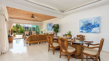 A spacious dining area with wicker furniture, a glass table, and artwork on the walls.